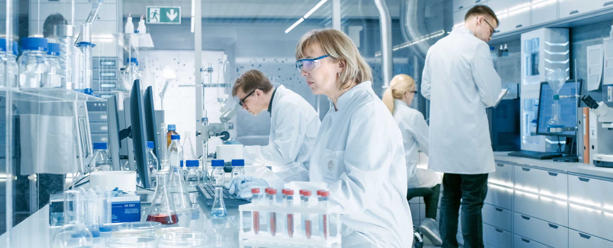 Female Scientist Analyzes Liquid in the Beaker and Types Down Ob AdobeStock 201606376 cropped scaled