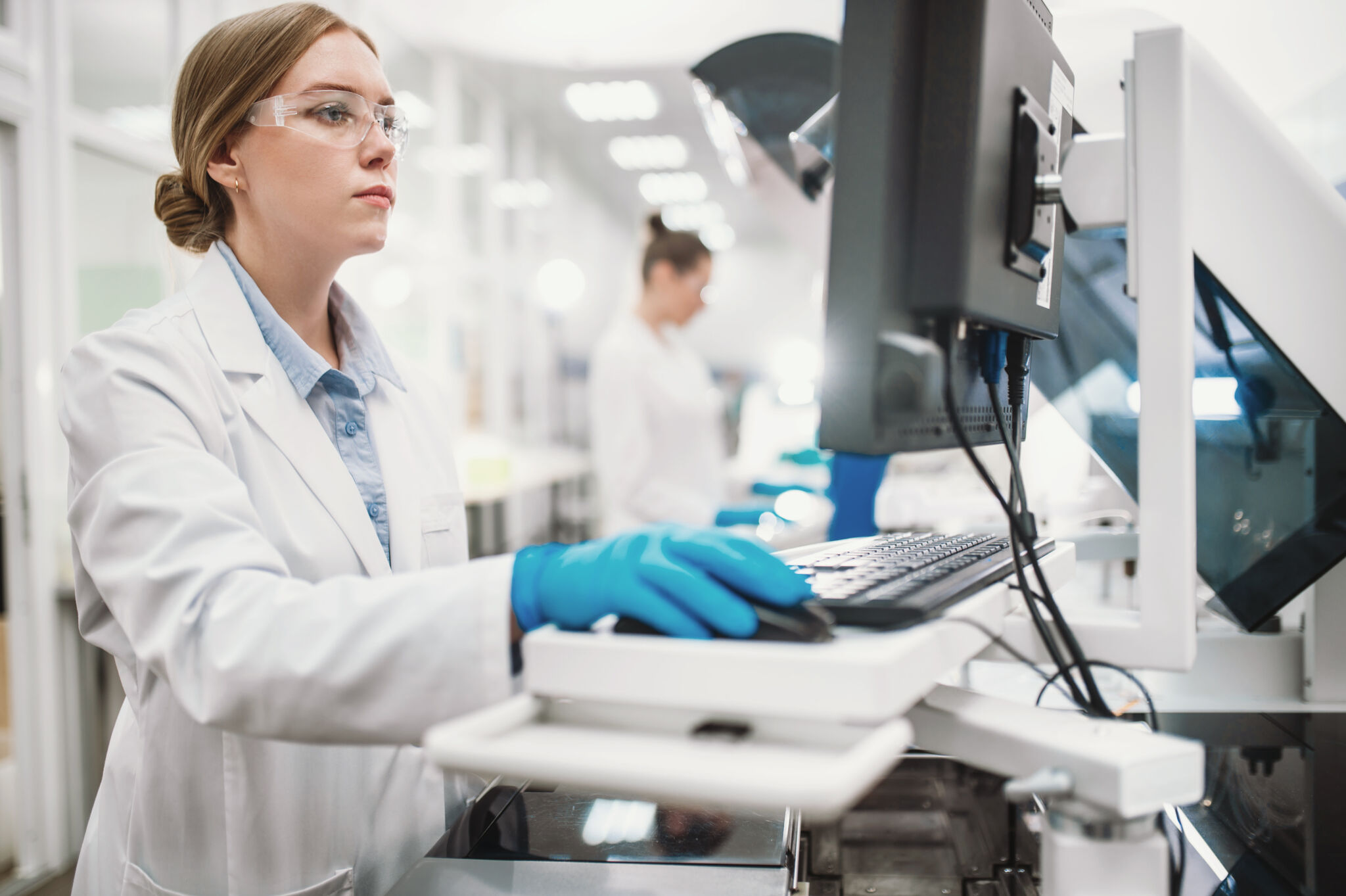 A team of laboratory technicians conduct a series of tests on a chemical analyzer in a biological laboratory. Two female scientists work in a modern equipped computer laboratory AdobeStock 685703561 scaled